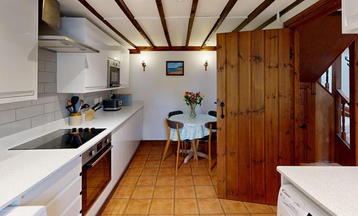 A spacious kitchen with beamed ceiling, modern appliances, and a round table with fresh flowers.